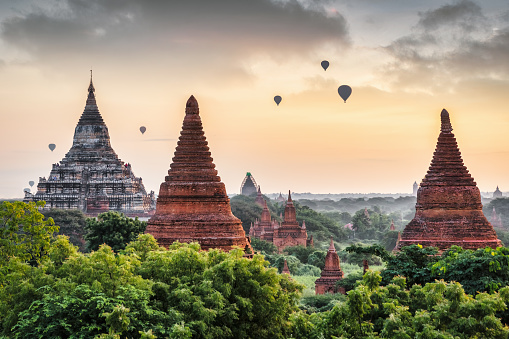 Myanmar Bagan Sunrise View over the majestic buddhist temples and temple pagodas in the ancient city of Bagan. Hot-Air Balloons starting their tourists flight over the Bagan Archaeological Zone. View from above towards the horizon over the ancient temple pagodas at dawn under moody colorful skyscape with flying hot air balloons. Bagan Archaeological Zone, Old Bagan, Bagan, Mandalay Region, Myanmar - Burma, Southeast Asia, Asia.