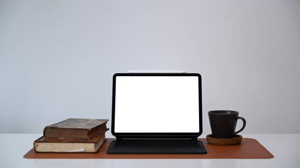 istock Front view of computer tablet, books and coffee cup on white office desk. 1308366853