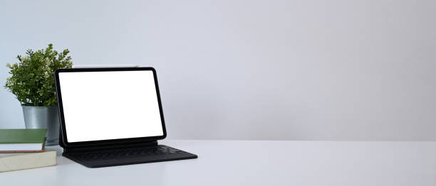 istock Mock up computer tablet with blank screen, house plant and books on white table. Copy space for products display montage. 1308366857
