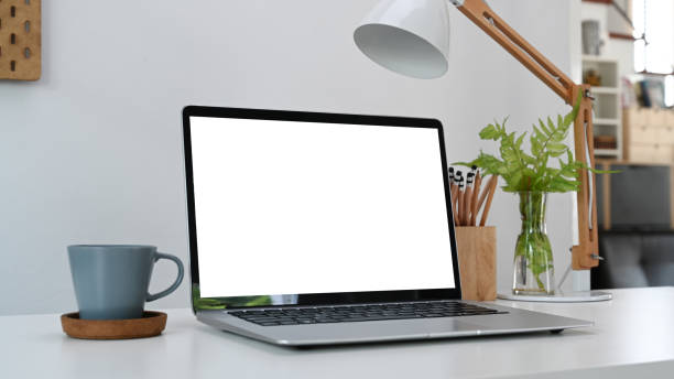 istock Mock up computer laptop with blank screen, coffee cup and pencils holder on white table at home office. 1308366864