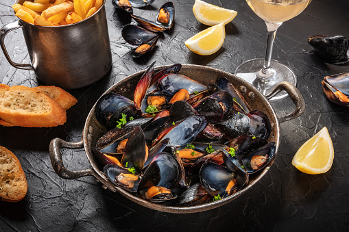 Mussels with wine, lemon, toasted bread and French fries, on a black background