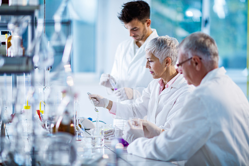 Senior female scientist analyzing chemical substances while working with her colleagues in laboratory.