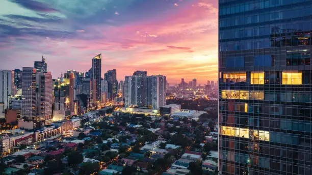 Makati Manila Sunset Panorama. Downtown Manila view over Makati District under colorful moody sunset light. Panorama view towards the Makati Skyscrapers ans setting Sun.. Partly illuminated modern skyscraper in the panorama foreground. Makati, Manila, Philippines, Southeast Asia, Asia