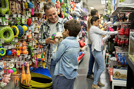 Caucasian man in mid 40s smiling at 9 year old son holding dog as they shop for toys and accessories.