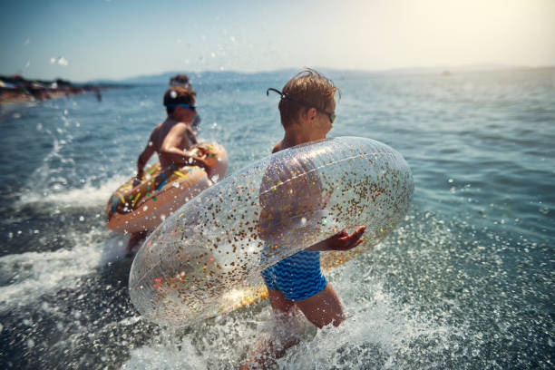 Kids having super fun running in the sea waves Brothers and sister are having fun in sea waves. Kids are running into incoming waves with inflatable rings and laughing.
Sunny summer day.
Nikon D850 inflatable ring photos stock pictures, royalty-free photos & images