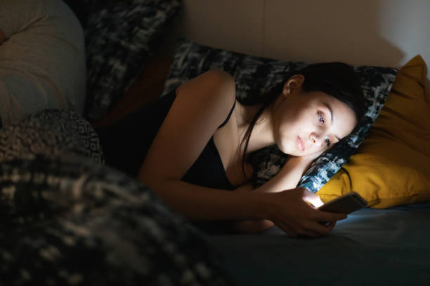 istock Young woman using smart phone in bed, staring at illuminated screen unable to fall asleep 1308376178