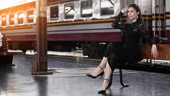 Fashion Asian Woman wear black luxury lace dress with glasses. LGBT Transgender model travels on train at station railway. Concept after post Covid