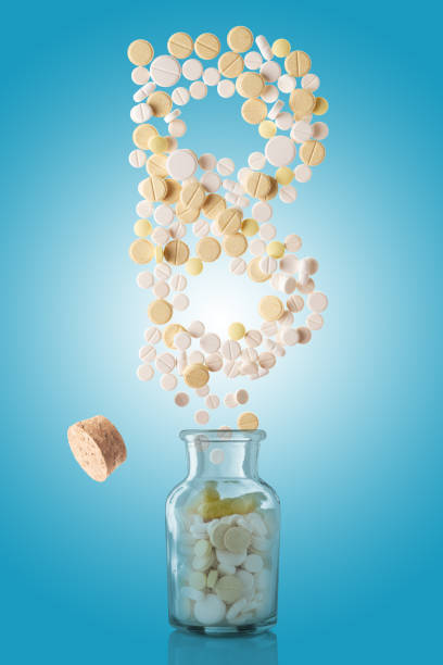 various pills fly out of a glass jar in the form of letter B, gradient blue background stock photo