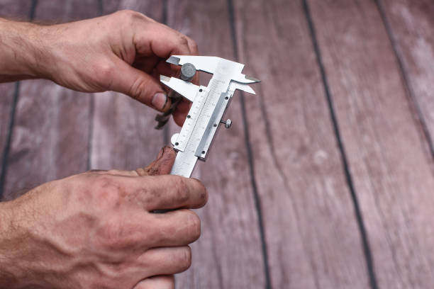 Measuring the drill diameter with a caliper Measuring the drill diameter with a caliper. Hands are dirty while working. Close-up. on a wooden background. micrometer screw gauge stock pictures, royalty-free photos & images