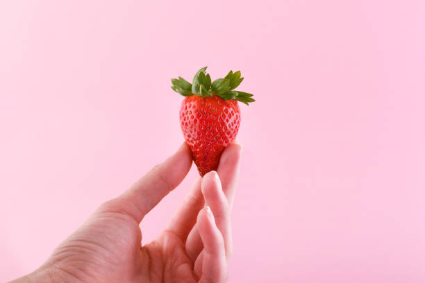 istock Woman's hand holds strawberry on pink background with copy space 1308382695
