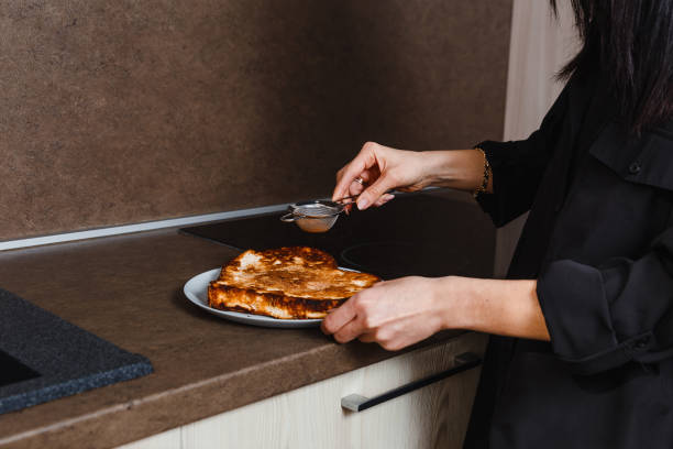 woman sprinkles cocoa powder with hot cake at home in kitchen