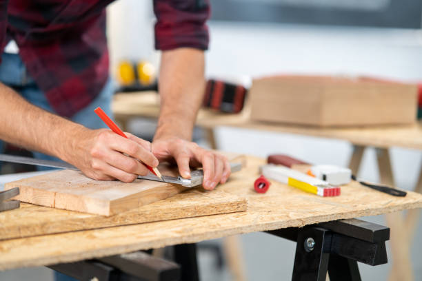 istock Close-up of a hardworking professional carpenter holding a angular ruler and pencil while measuring a board in a carpentry workshop. A bearded DIY enthusiast measures wood. There are a locksmith table and tools in the background 1308386743