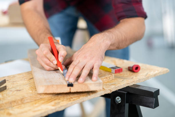Close-up of a hardworking professional carpenter holding a ruler and pencil while measuring a board in a carpentry workshop. A bearded DIY enthusiast measures wood. There are a locksmith table and tools in the background