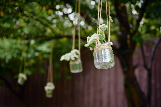 istock Rustic wedding decorations with flowers in glass jar hanging on green tree outdoors, copy space. Floral arrangement. Wedding concept 1308387457