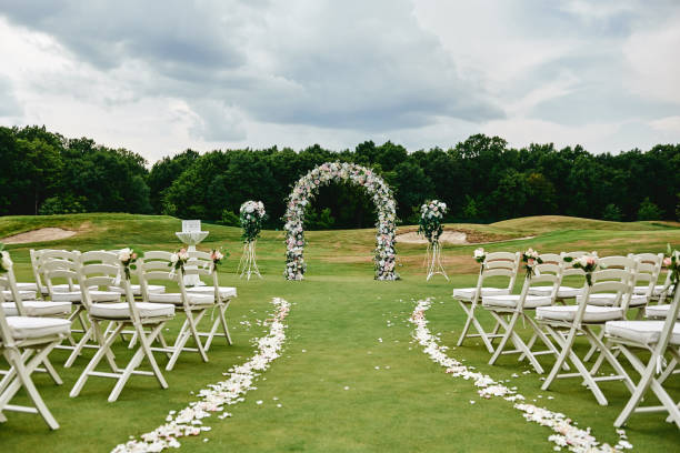 istock Place for wedding ceremony on green golf course, copy space. Wedding arch decorated with flowers and white chairs on each side of archway outdoors. Wedding setting 1308387522