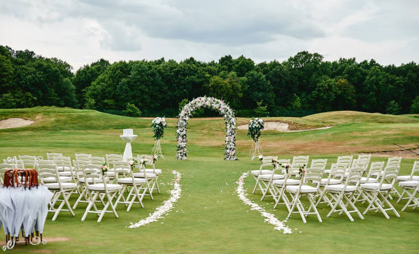 luogo per la cerimonia nuziale sul campo da golf verde, spazio di copia. arco nuziale decorato con fiori e sedie bianche su ciascun lato dell'arco all'aperto. impostazione del matrimonio - wedding venue foto e immagini stock