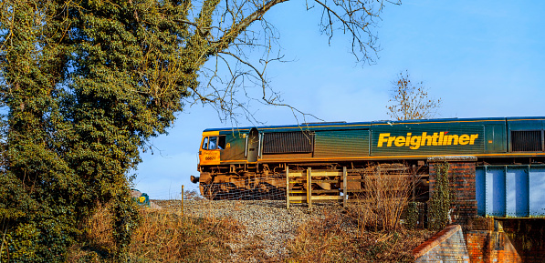 March 22nd. 2021. A freightliner locomotive is pulling a goods / freight train over a railway bridge. Lapworth, Warwickshire, England UK. It is a sunny day in Spring and there are no people in the picture.