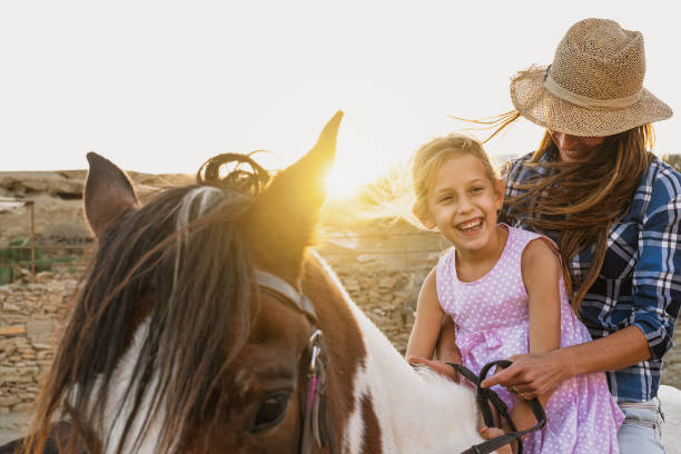 mère et descendant heureux de famille ayant le cheval d’équitation d’équitation d’amusement à l’intérieur du ranch - mode de vie rural photos et images de collection