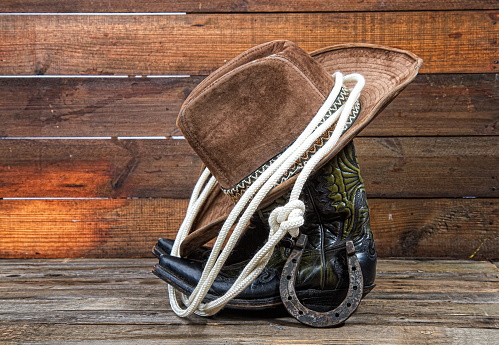 Shabby old ornate classic cowboy boots hat and lasso on wooden background