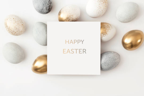 istock Golden and gray eggs with a paper white card on a white background. Minimal easter concept. 1308391947