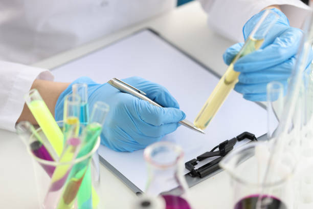 Scientist chemist holding test tube with yellow liquid in his hands and writing in documents closeup. Food quality assessment concept
