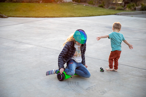 A brother and sister play outside on a hoverboard