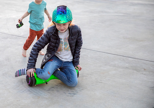 A brother and sister play outside on a hoverboard