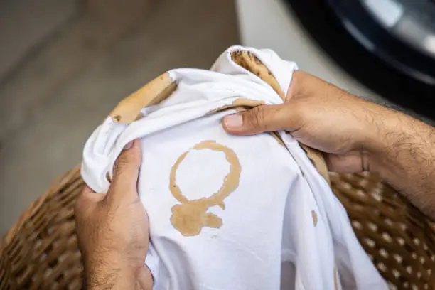 Photo of White cotton shirt A lot of stains, stains, coffee stains, man's hand holds the shirt up and spreads it to look dirty Must be brought to the washing machine
