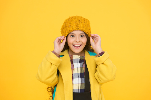 Winter hat accessory. Girl long hair yellow background. Cold season concept. Winter fashion accessory. Small child wearing warm hat. Choose between cutest and trendiest. Kid girl wear knitted hat.