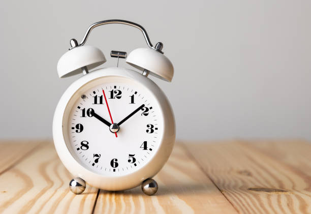 istock Small white alarm clock, black numbers, set the time for 10.10 o'clock, placed on a wood table. 1308396273