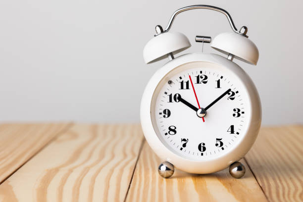 istock Small white alarm clock, black numbers, set the time for 10.10 o'clock, placed on a wood table. 1308396283