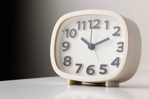 istock Small white alarm clock, black numbers, set the time for 10.10 o'clock, placed on a white table. 1308396284