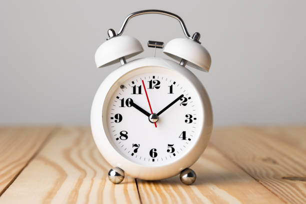 istock Small white alarm clock, black numbers, set the time for 10.10 o'clock, placed on a wood table. 1308396316