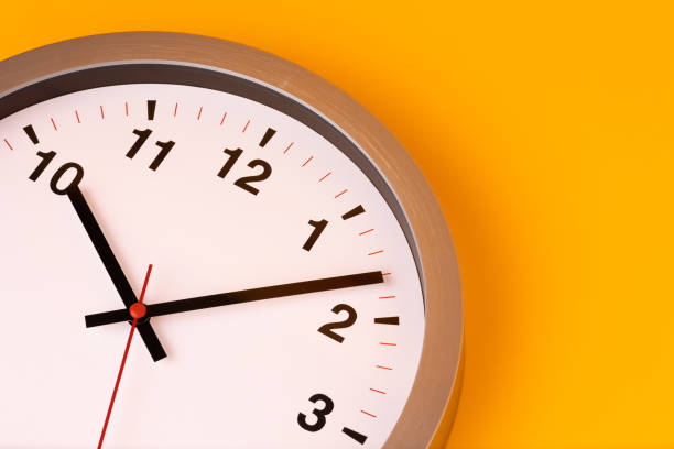 istock Large white alarm clock, black numbers, set the time placed on a table. Clock on isolated yellow background. 1308396454