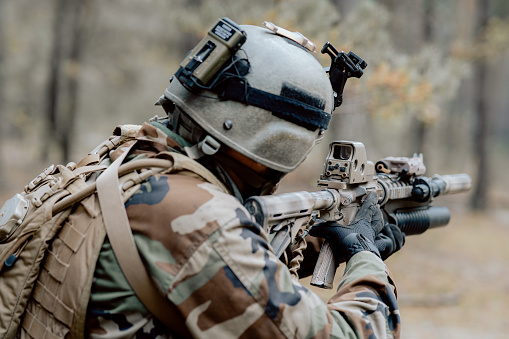 A soldier in a special military uniform, with a helmet on his head and with a sniper rifle in the forest, aiming through a scope.
