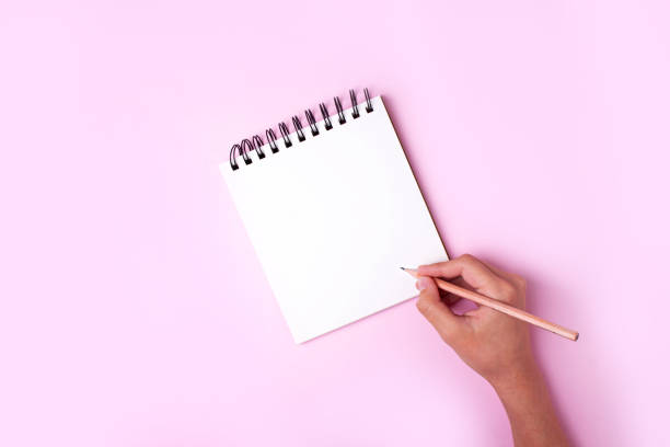 istock Hand writes with a pencil in a notebook on a pink background. Concept too doo list 1308397979