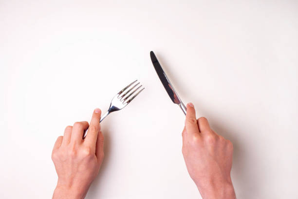 istock Hands hold a knife with a fork on a white table isolated. View from above 1308397993