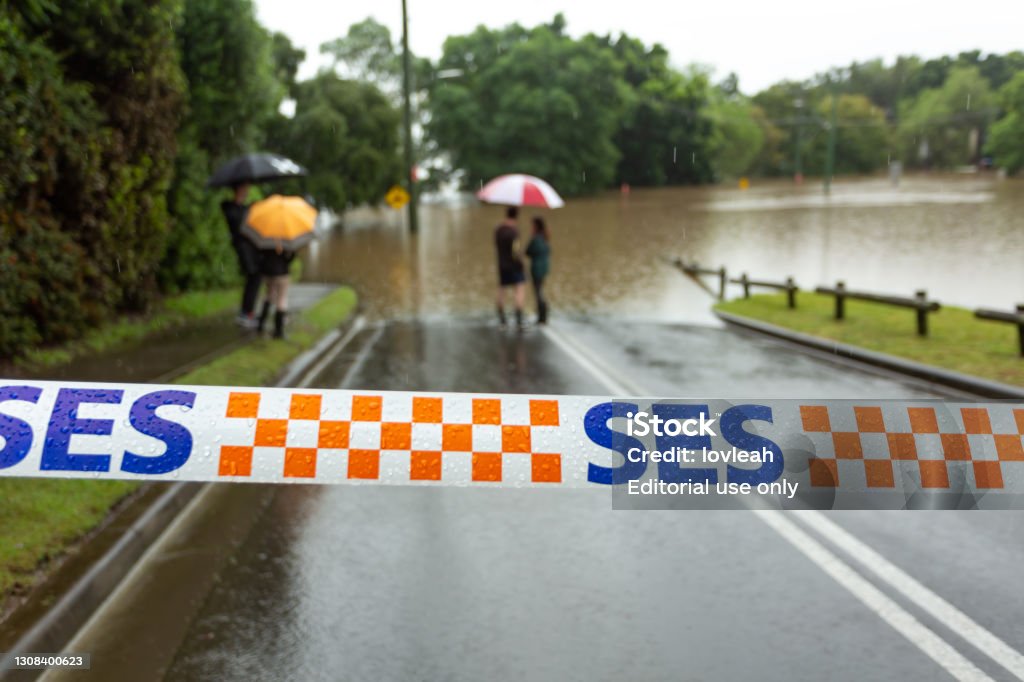 Windsor, Australia - March 22, 2021;  SES tape across a flooded road in Windsor Windsor, Australia - March 22, 2021; SES (State Emergency Services) tape stretched across a flooded road as locals look on.  Extreme weather caused flooding not seen in over 50 years. Flood Stock Photo