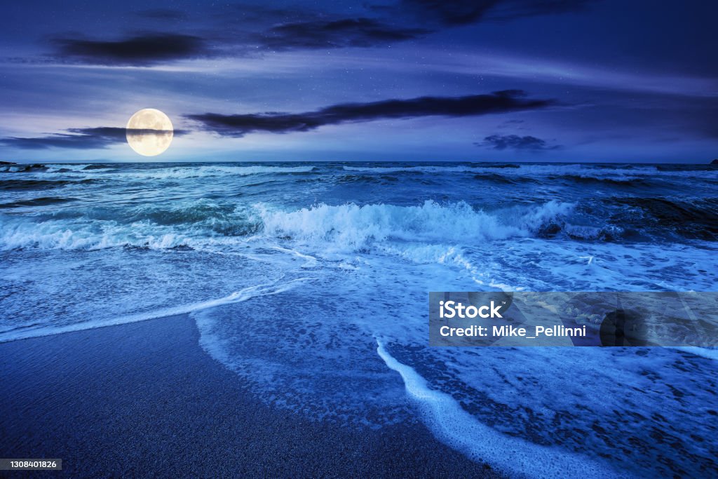 sea tide on a cloudy night sea tide on a cloudy sunrise. green waves crashing golden sandy beach in full moon light. storm weather approaching. summer holiday concept Tide Stock Photo