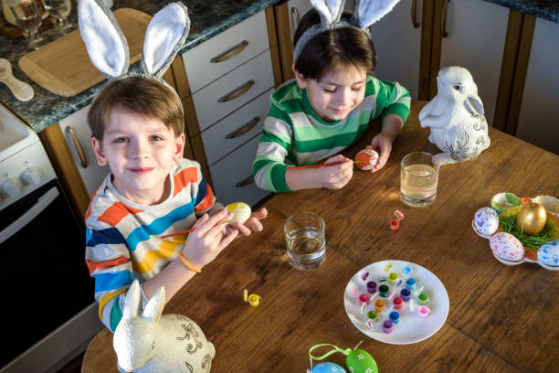 屋内、家庭のキッチンでイースター休暇のための卵を着色する2人の小さな子供の男の子。兄弟兄弟は楽しみを持って、ごちそうを祝います。トップビュー - easter easter bunny fun humor ストックフォトと画像