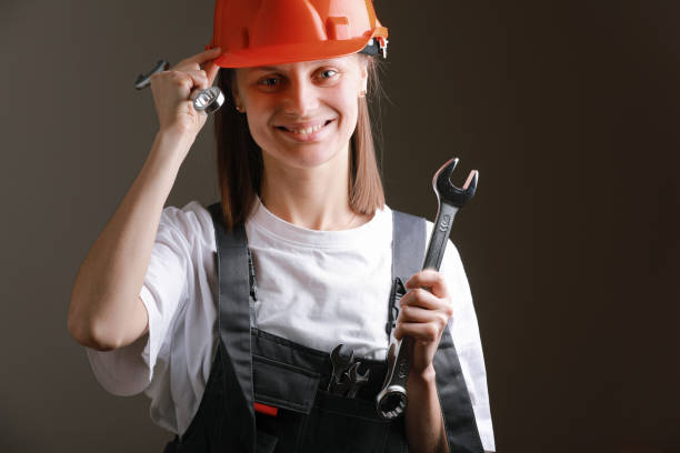 istock Young beautiful girl engineer in a gray uniform and protective helmet smiles with tools, wrenches in her hands. Equality between men and women. Repairwoman posing on a gray background. labor day 1308404640