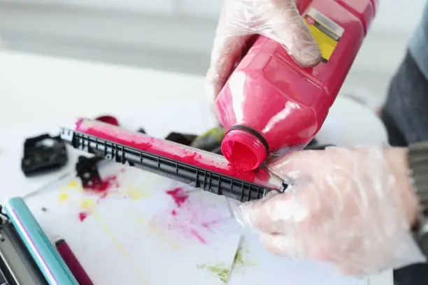 Photo of Technician pours red ink into cartridge closeup