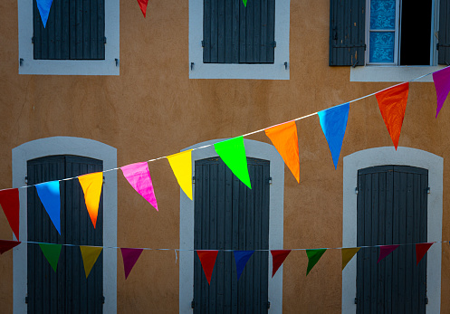 multi colour  celebration flags or bunting hanging in french street with colorful facade and shutters ,focus on flags .