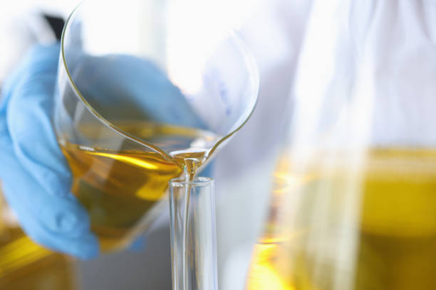 Scientist pours clear golden liquid into glass flask