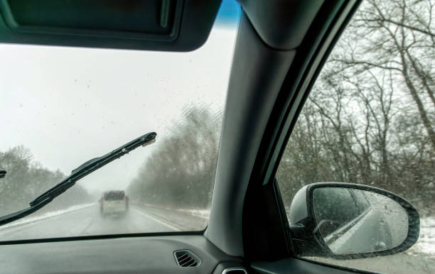 car wipers wiping the windshield. winter highway during snowfall - snow driving side view mirror rain imagens e fotografias de stock
