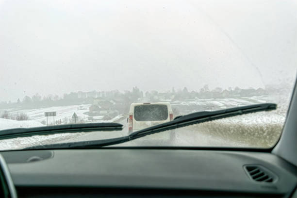car wipers wiping the windshield. winter highway during snowfall - snow driving side view mirror rain imagens e fotografias de stock