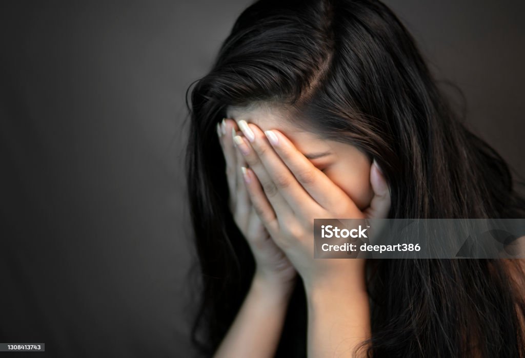 Portrait of stress young woman covering her face with hands and crying. Close-up portrait of alone, stressed young woman sitting in darkness and crying with covering her face with hands. Women Stock Photo