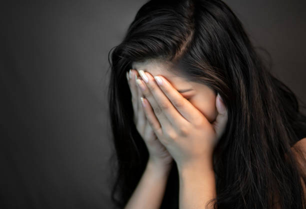 Portrait of stress young woman covering her face with hands and crying. Close-up portrait of alone, stressed young woman sitting in darkness and crying with covering her face with hands. crying stock pictures, royalty-free photos & images