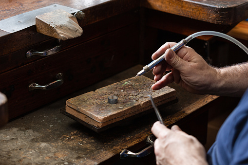 goldsmith jeweler soldering a silver ring on the workbench with a soldering iron and clamping it on top of a ceramic brick. caucasian man in the jewelry workshop.