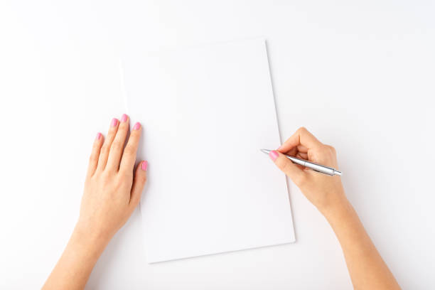 istock Woman’s hands writing with pen over blank paper isolated on white background. Top view 1308415952